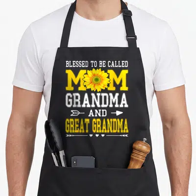 Blessed mother's day aprons - Sunflower graphic with stacked text Blessed to Be Called Mom Grandma and Great Grandma — shown on a black cotton canvas apron against a white background