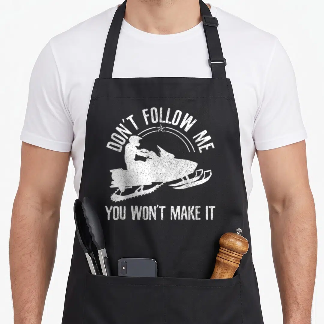 Motor snowmobile girl apron - White distressed snowmobile silhouette with Don't Follow Me text and star accent — shown on a black cotton canvas apron against a white background
