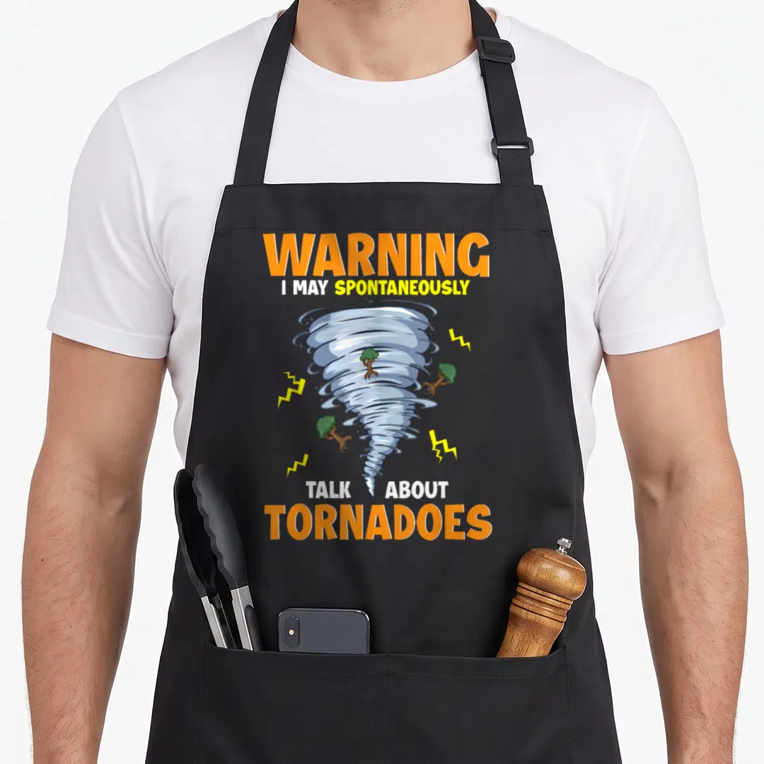 May talk apron - Cartoon tornado with scattered trees lightning bolts and stacked warning text in orange blue yellow — shown on a black cotton canvas apron against a white background
