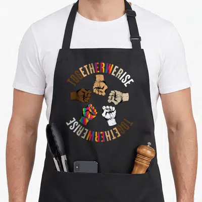 Together social life apron - Five fists in brown tan white and rainbow colors surrounding arched TOGETHERWERISE text — shown on a black cotton canvas apron against a white background