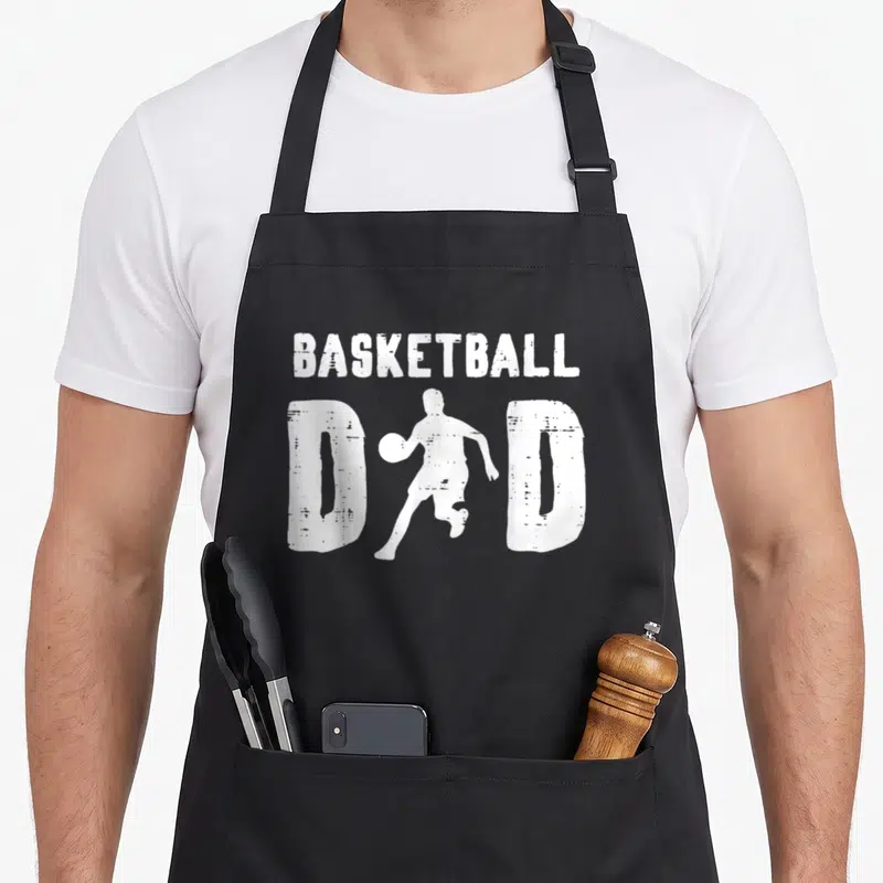 Basketball daddy apron - White basketball player silhouette integrated into the word DAD with BASKETBALL above — shown on a black cotton canvas apron against a white background