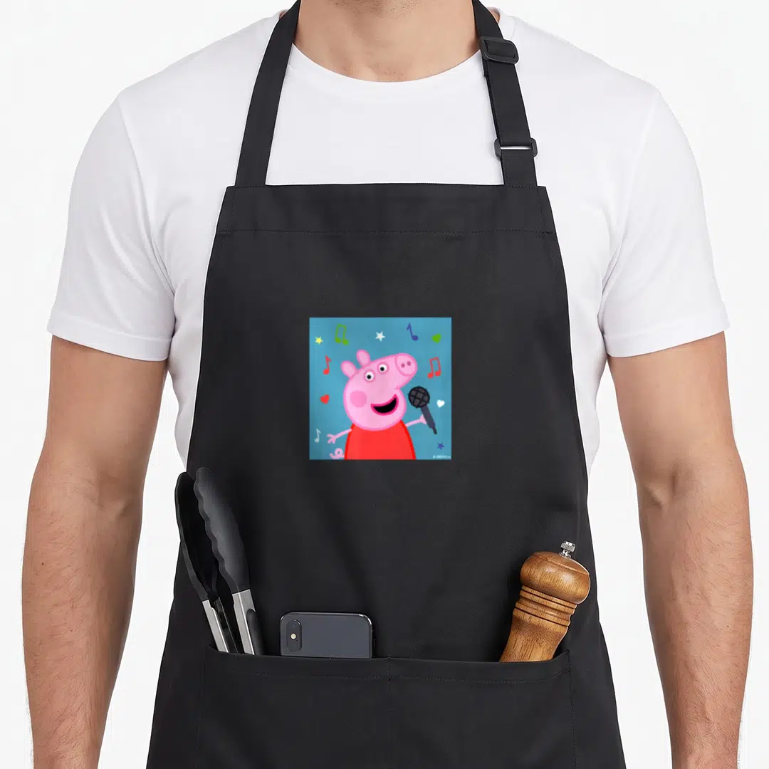Music pig apron - Pink pig holding microphone surrounded by musical notes and hearts on blue — shown on a black cotton canvas apron against a white background