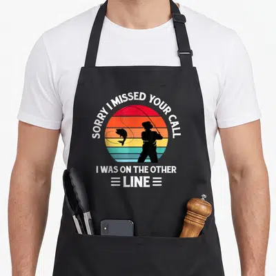 Missed fishing aprons - Retro sun with fisherman silhouette and SORRY I MISSED YOUR CALL text — shown on a black cotton canvas apron against a white background