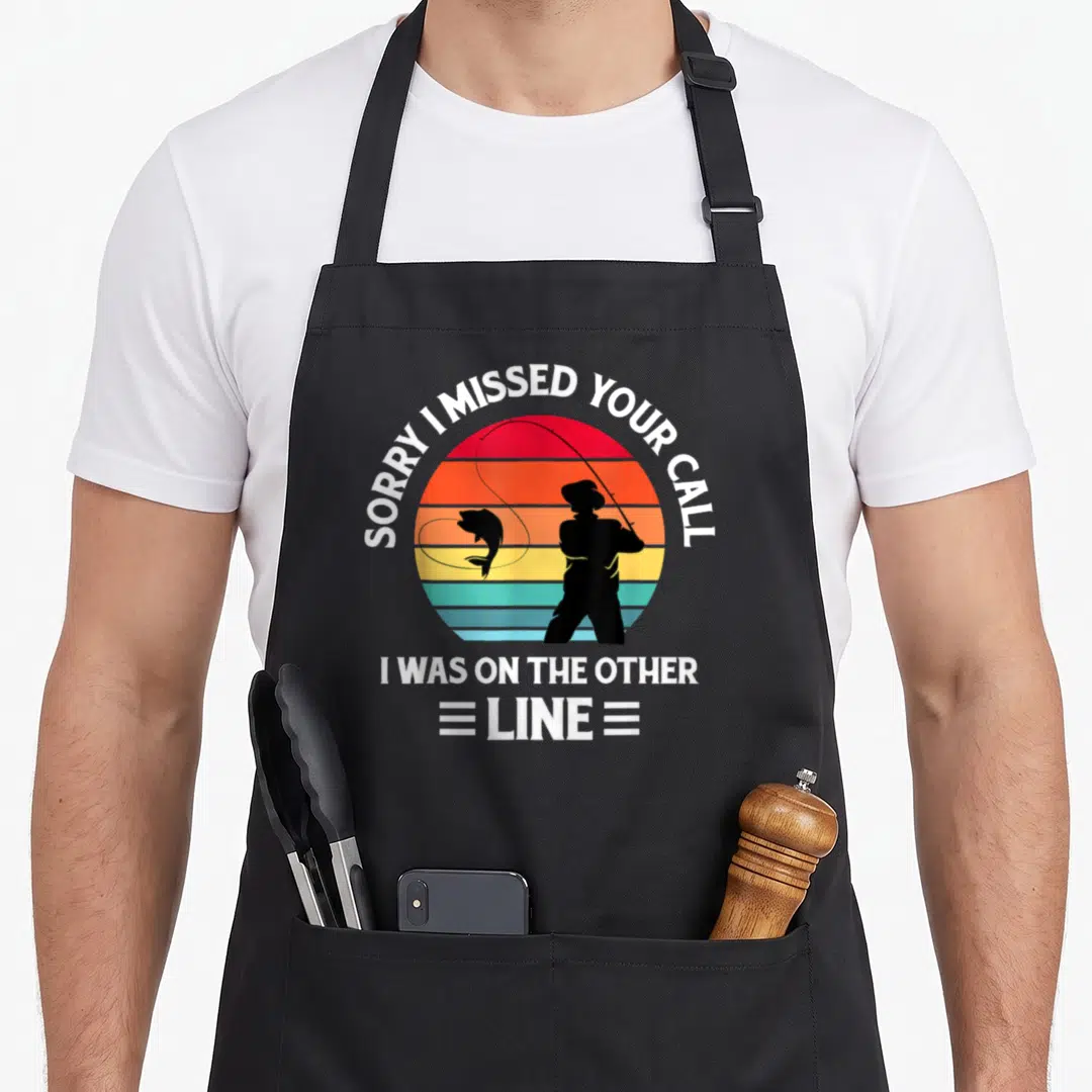 Missed fishing aprons - Retro sun with fisherman silhouette and SORRY I MISSED YOUR CALL text — shown on a black cotton canvas apron against a white background