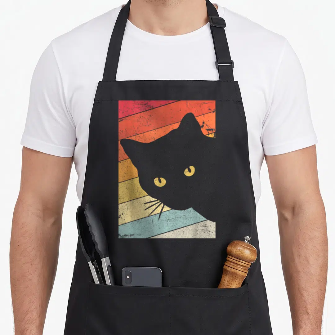 Funny animal cat apron - Grey cat silhouette with yellow eyes over diagonal red orange yellow and blue stripes — shown on a black cotton canvas apron against a white background