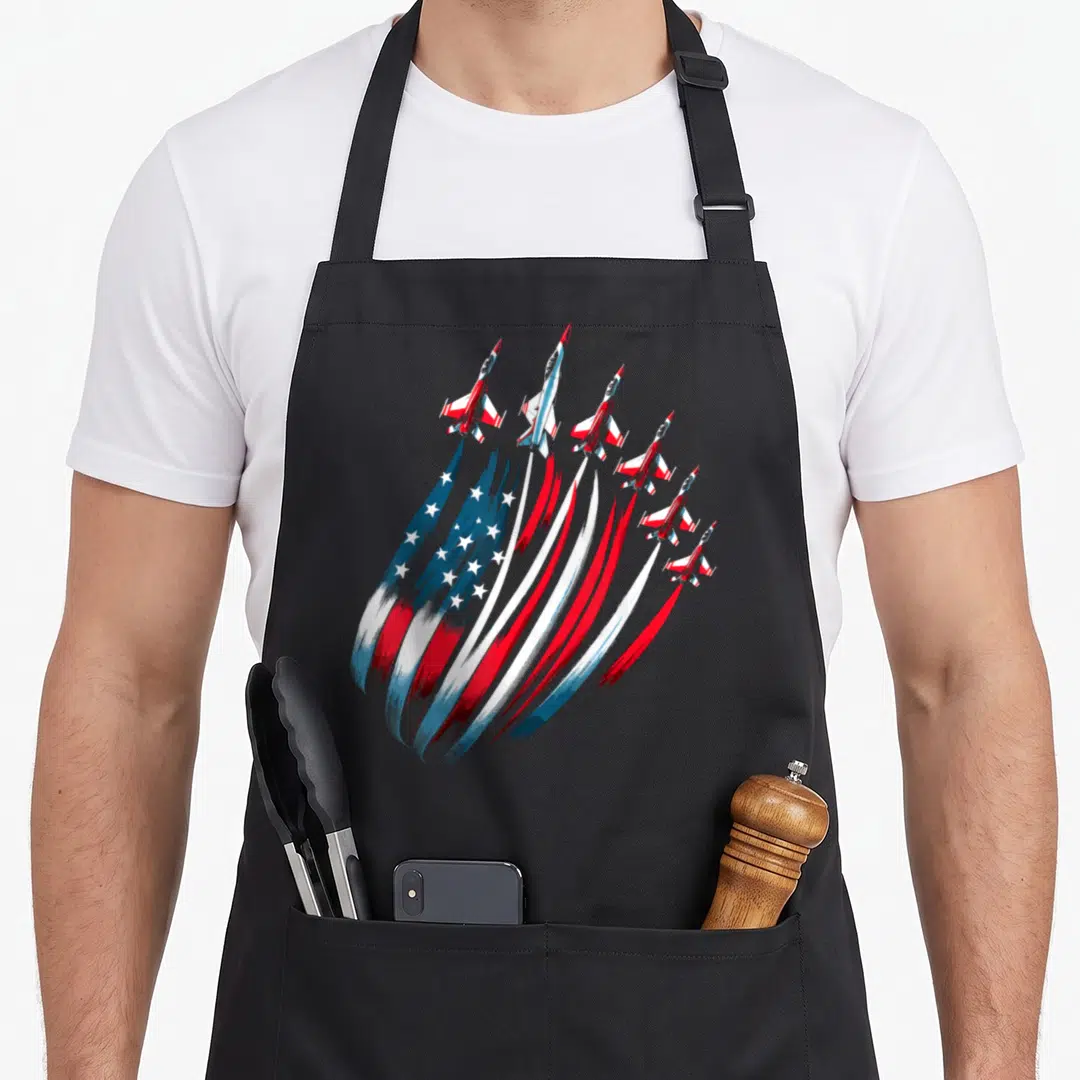 Jet 4th of july apron - Six red white and blue jets flying upward leaving smoke trails shaped like the US flag stars — shown on a black cotton canvas apron against a white background