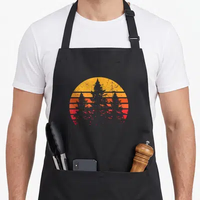 Pine minimalist apron - Retro circular sunset with horizontal yellow orange red grey bands and centered pine tree — shown on a black cotton canvas apron against a white background
