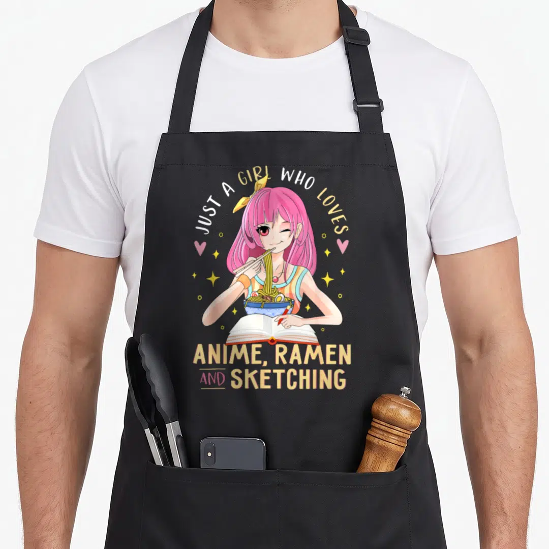 Funny ramen sketching anime apron - Pink anime girl eating ramen and sketching with arched text and stars — shown on a black cotton canvas apron against a white background