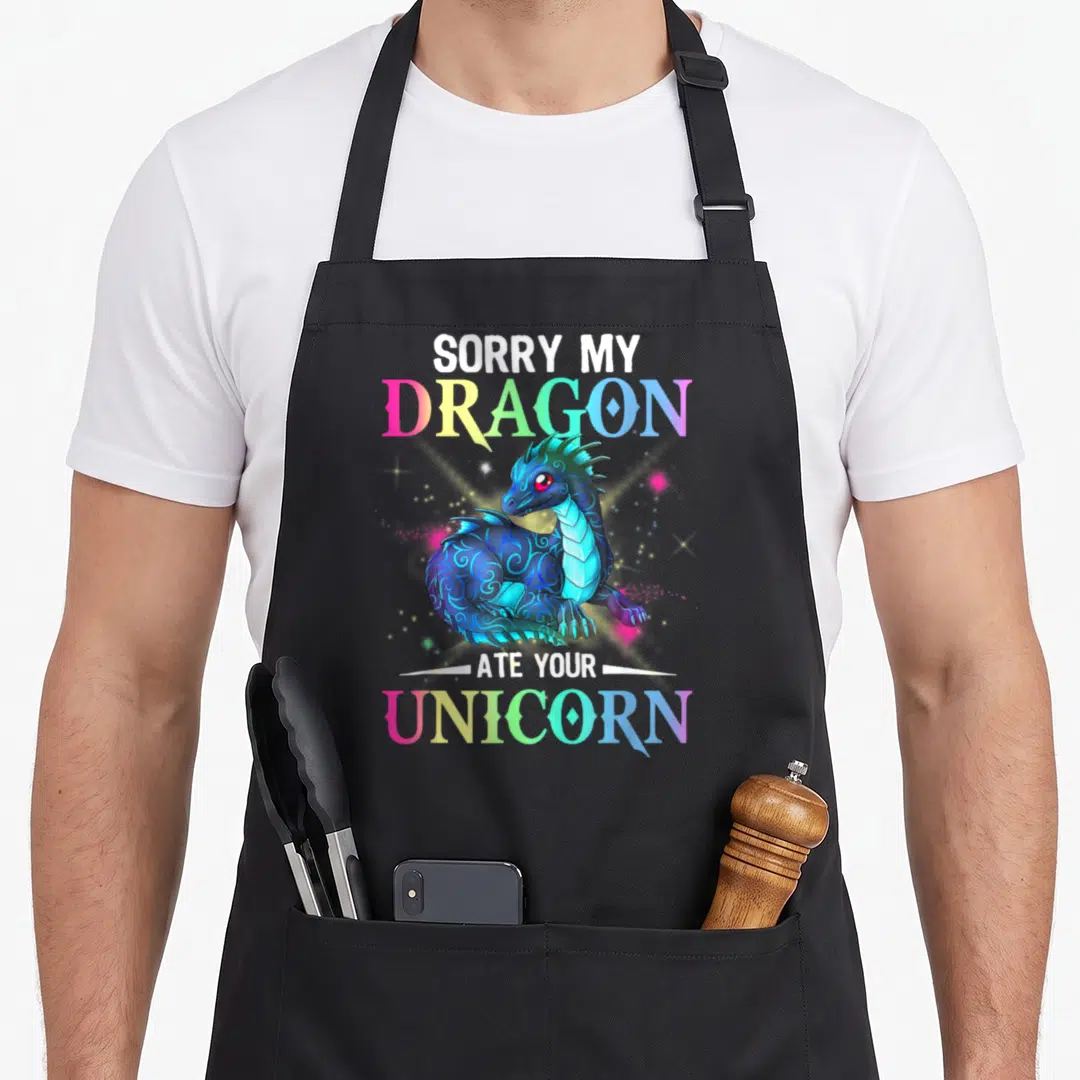 Sorry dragon apron - Blue cartoon dragon with SORRY MY DRAGON ATE YOUR UNICORN text in rainbow gradients — shown on a black cotton canvas apron against a white background
