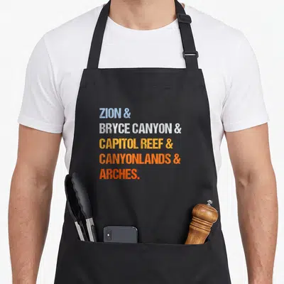 National utah girl apron - Stacked text reading ZION, BRYCE CANYON, CAPITOL REEF, CANYONLANDS, ARCHES in blue, white — shown on a black cotton canvas apron against a white background