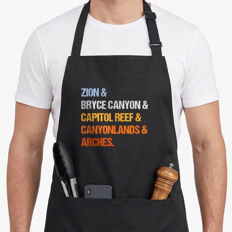 National utah girl apron - Stacked text reading ZION, BRYCE CANYON, CAPITOL REEF, CANYONLANDS, ARCHES in blue, white — shown on a black cotton canvas apron against a white background