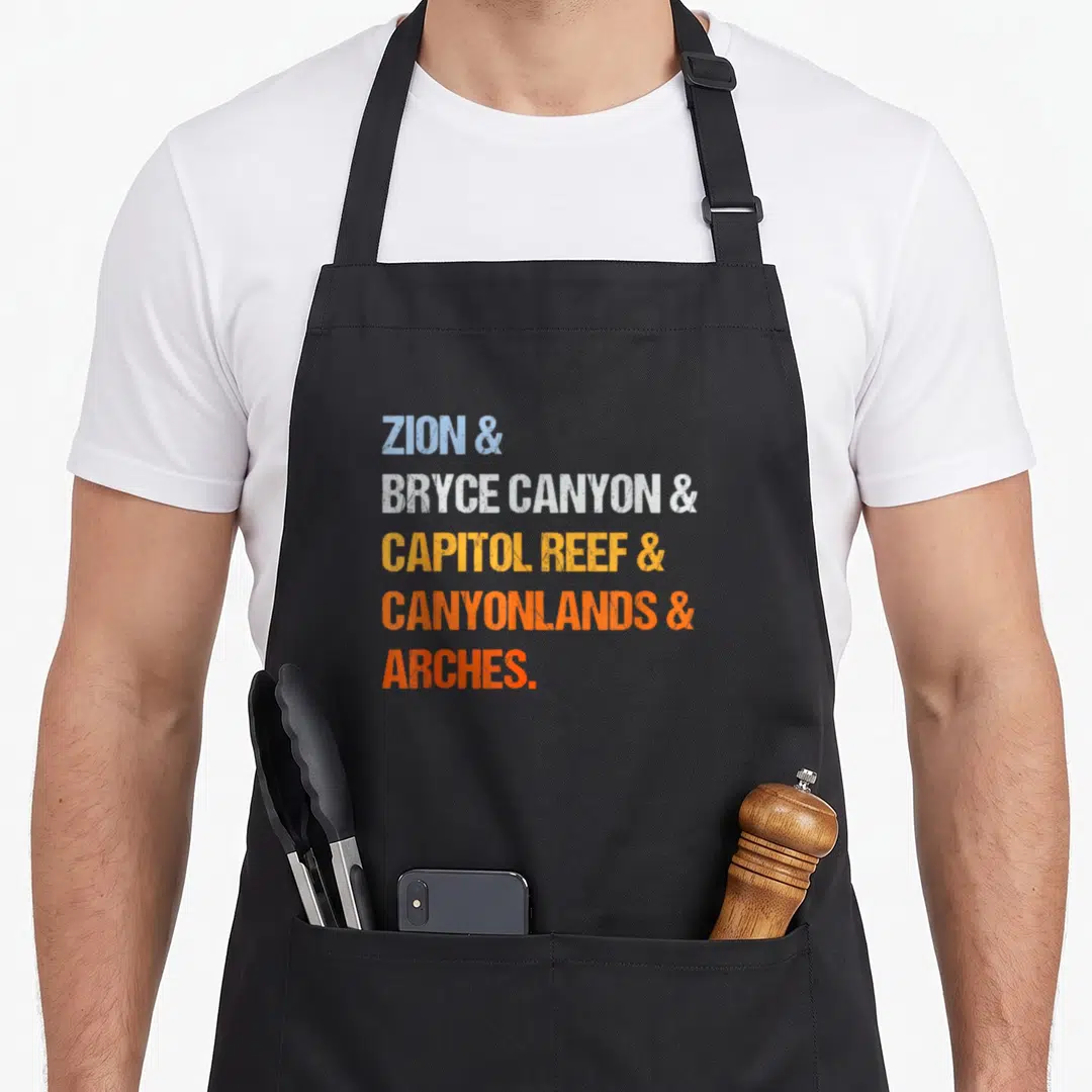 National utah girl apron - Stacked text reading ZION, BRYCE CANYON, CAPITOL REEF, CANYONLANDS, ARCHES in blue, white — shown on a black cotton canvas apron against a white background