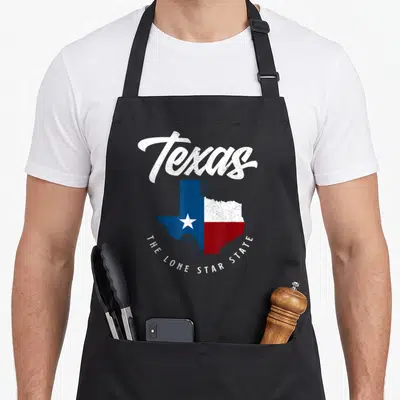 Texas texans apron - Distressed Texas map with Lone Star flag colors and curved text below — shown on a black cotton canvas apron against a white background
