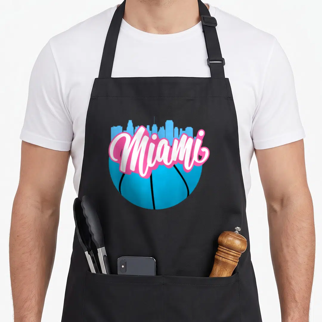 Cityscape florida apron - Blue basketball with light blue skyline and white Miami text outlined in pink — shown on a black cotton canvas apron against a white background
