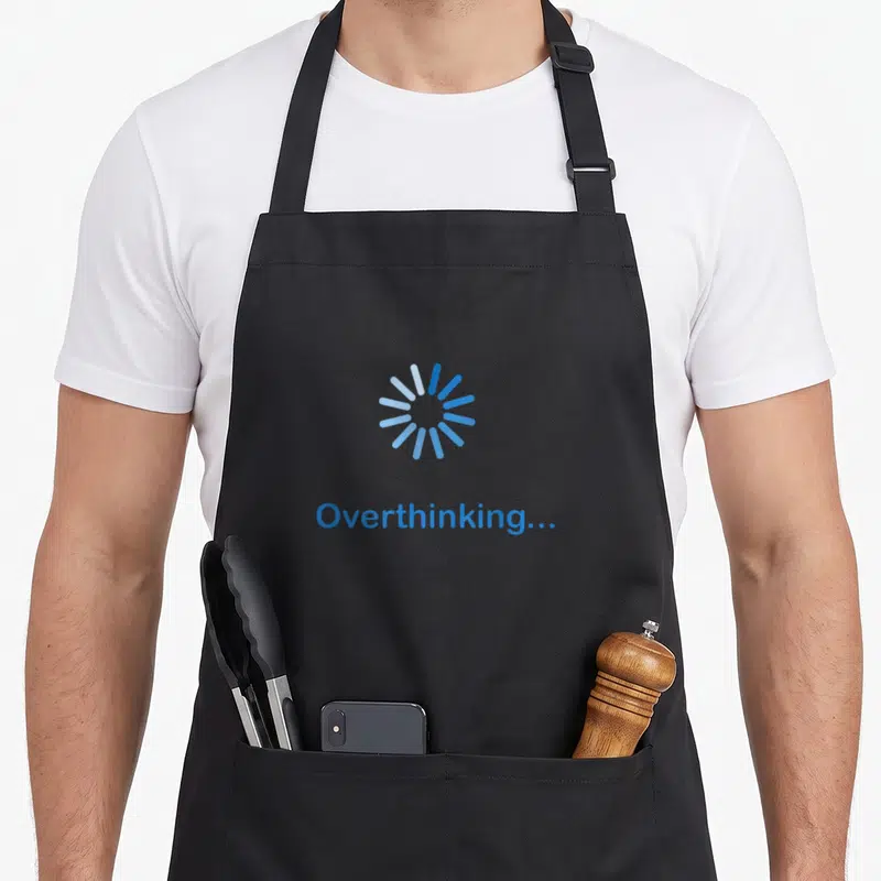 Overthinking antisocial apron - Blue loading spinner icon above the word Overthinking on a black background — shown on a black cotton canvas apron against a white background