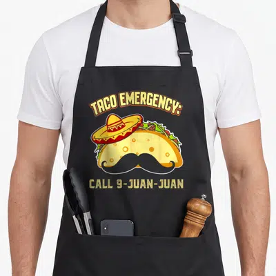 Emergency mexican apron - Cartoon taco wearing sombrero and mustache with TACO EMERGENCY CALL 9-JUAN-JUAN text — shown on a black cotton canvas apron against a white background