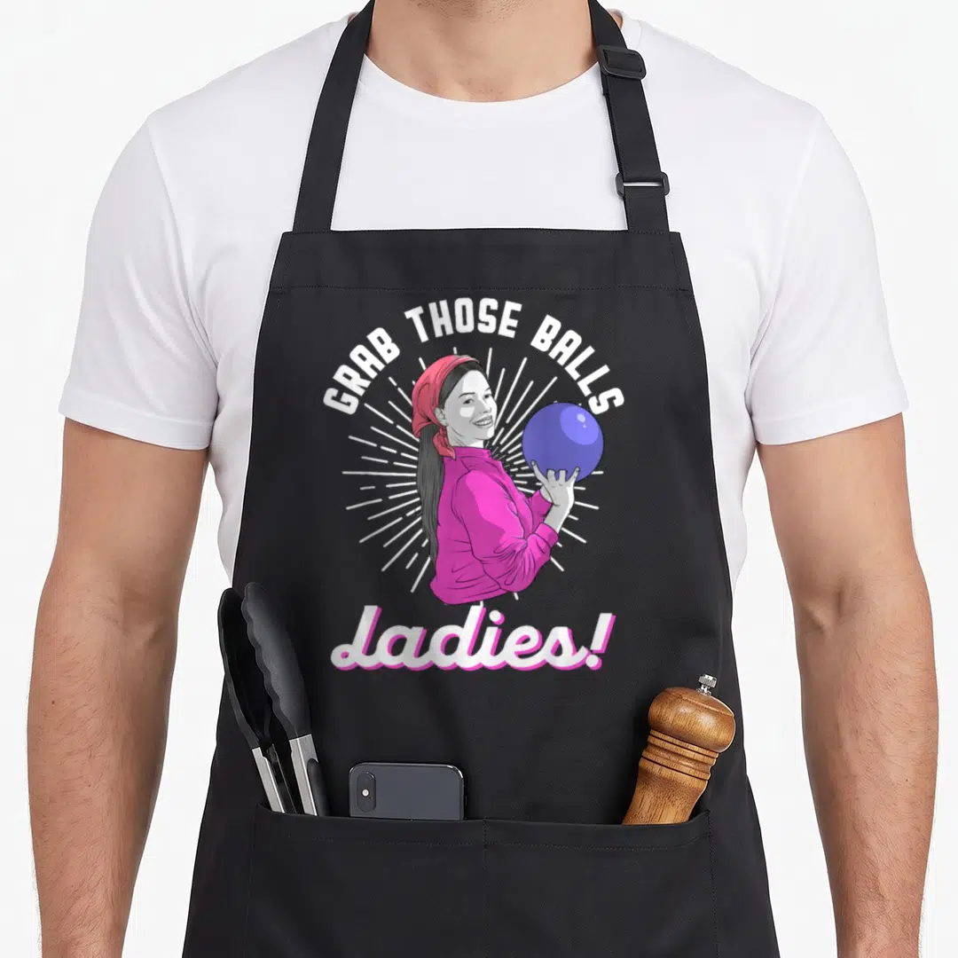 Grab bowling player apron - Cartoon woman in pink holding purple ball with GRAB THOSE BALLS Ladies text — shown on a black cotton canvas apron against a white background