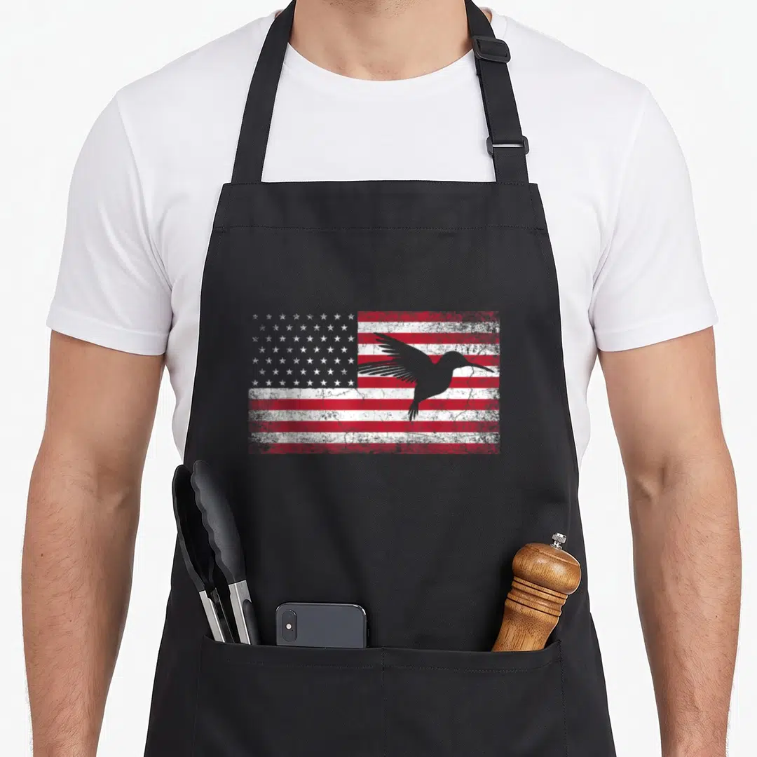 Hummingbird 4th of july apron - Grey hummingbird silhouette over distressed red white American flag — shown on a black cotton canvas apron against a white background