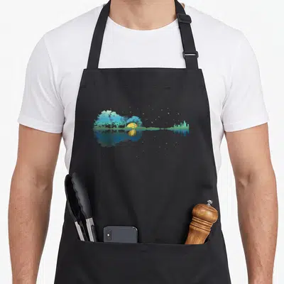 Guitar sky apron - Symmetrical landscape with blue trees, yellow sun, and starry reflection in water — shown on a black cotton canvas apron against a white background