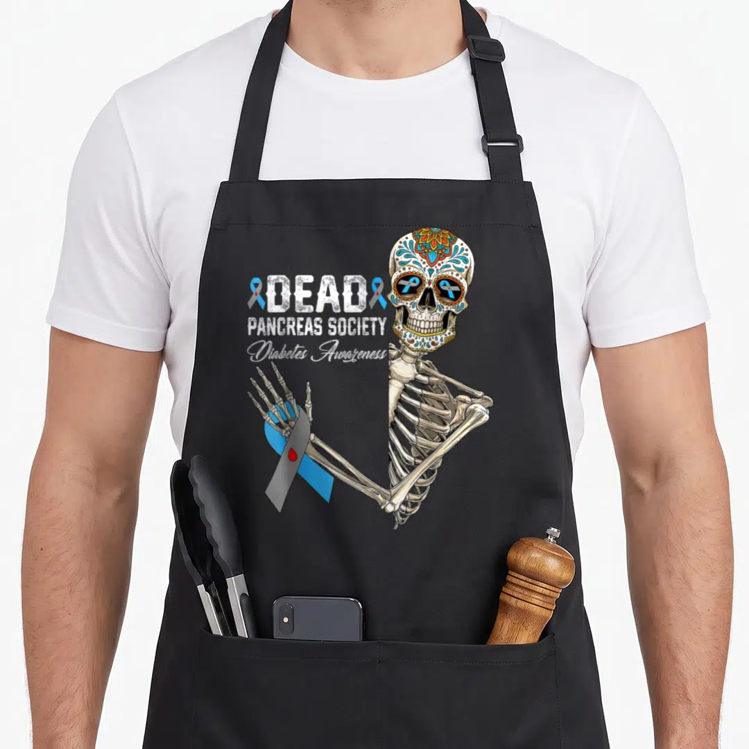 Pancreas day of the dead apron - Half skeleton with sugar skull holding blue ribbon with red drop next to stacked text — shown on a black cotton canvas apron against a white background