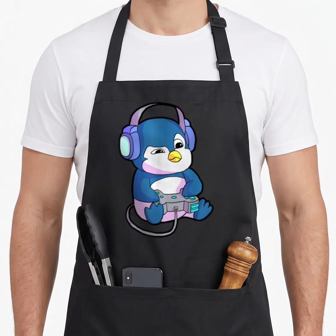 Gamer penguin aprons - Blue cartoon penguin sitting with purple headphones and grey game controller — shown on a black cotton canvas apron against a white background