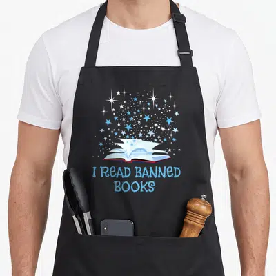Read banned nerd apron - Open book with blue and white stars and text I READ BANNED BOOKS — shown on a black cotton canvas apron against a white background