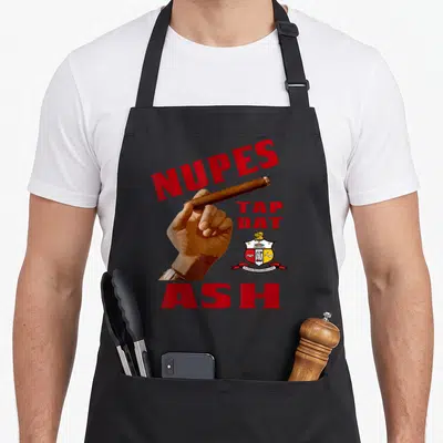 Nupe tap apron - Brown hand holding cigar with red NUPES TAP DAT ASH text and crest on black background — shown on a black cotton canvas apron against a white background