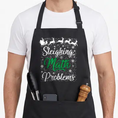Sleighing xmas apron - Sleiving Math Problems text with Santa sleigh and math formulas — shown on a black cotton canvas apron against a white background