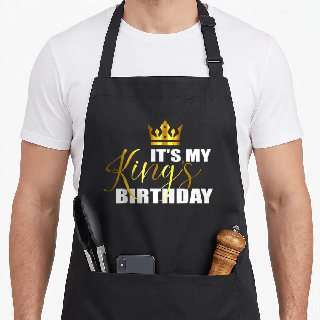 Birthday squad kings apron - Gold crown above IT'S MY King's BIRTHDAY text in white and gold typography — shown on a black cotton canvas apron against a white background
