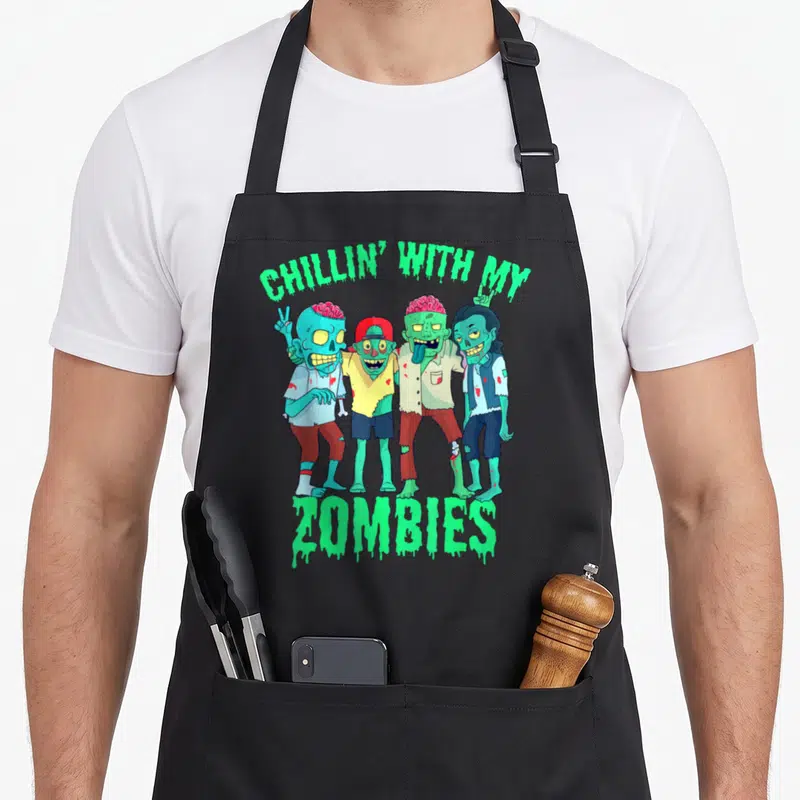 Chillin zomby halloween apron - Four cartoon zombies with neon green text and red blood splatters — shown on a black cotton canvas apron against a white background
