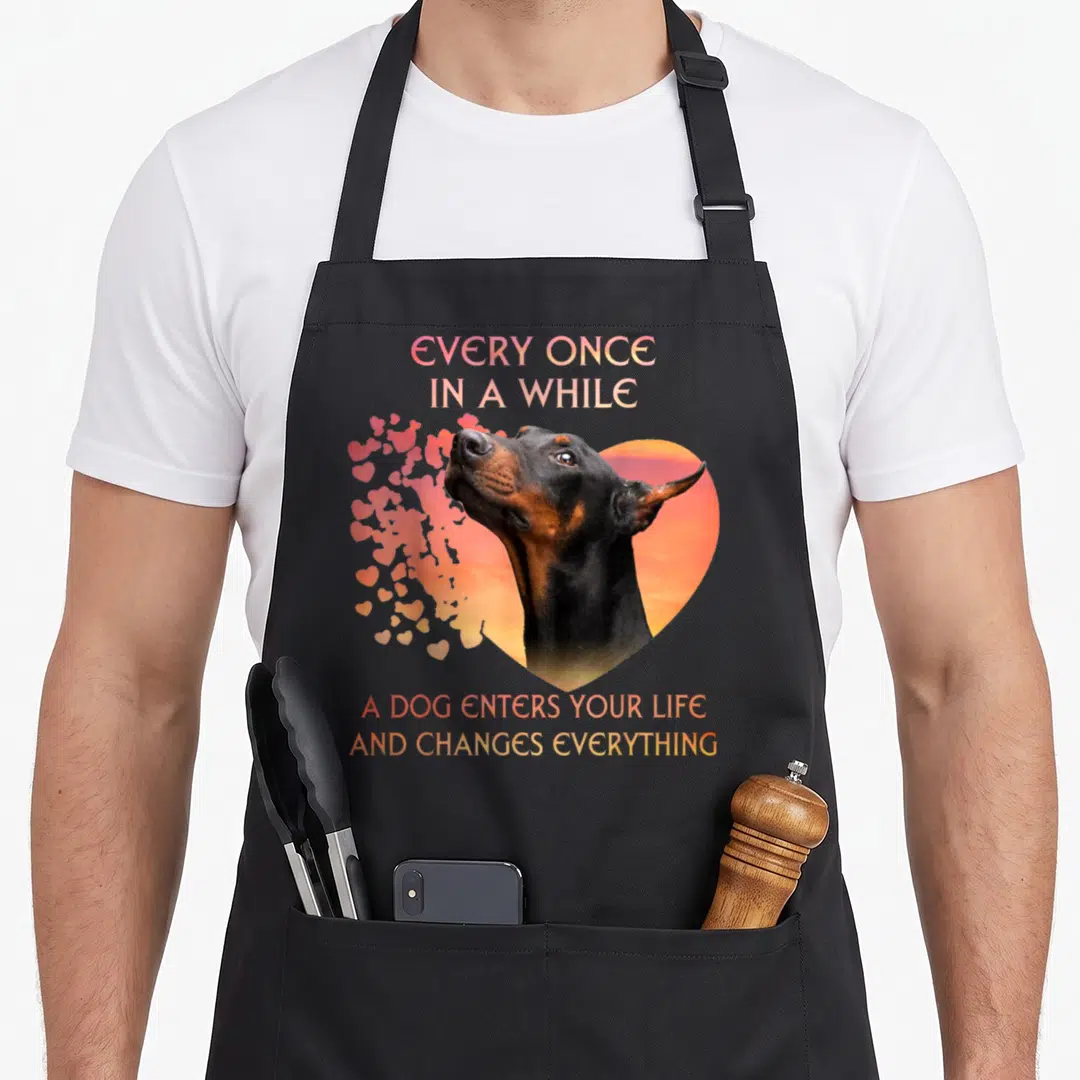 Once dog apron - Doberman head inside orange heart with floating pink hearts and gradient text — shown on a black cotton canvas apron against a white background