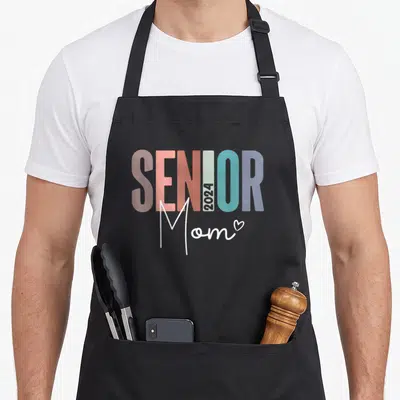 Class senior apron for women - Senior 2024 Mom text art in pink orange teal purple and white with heart — shown on a black cotton canvas apron against a white background