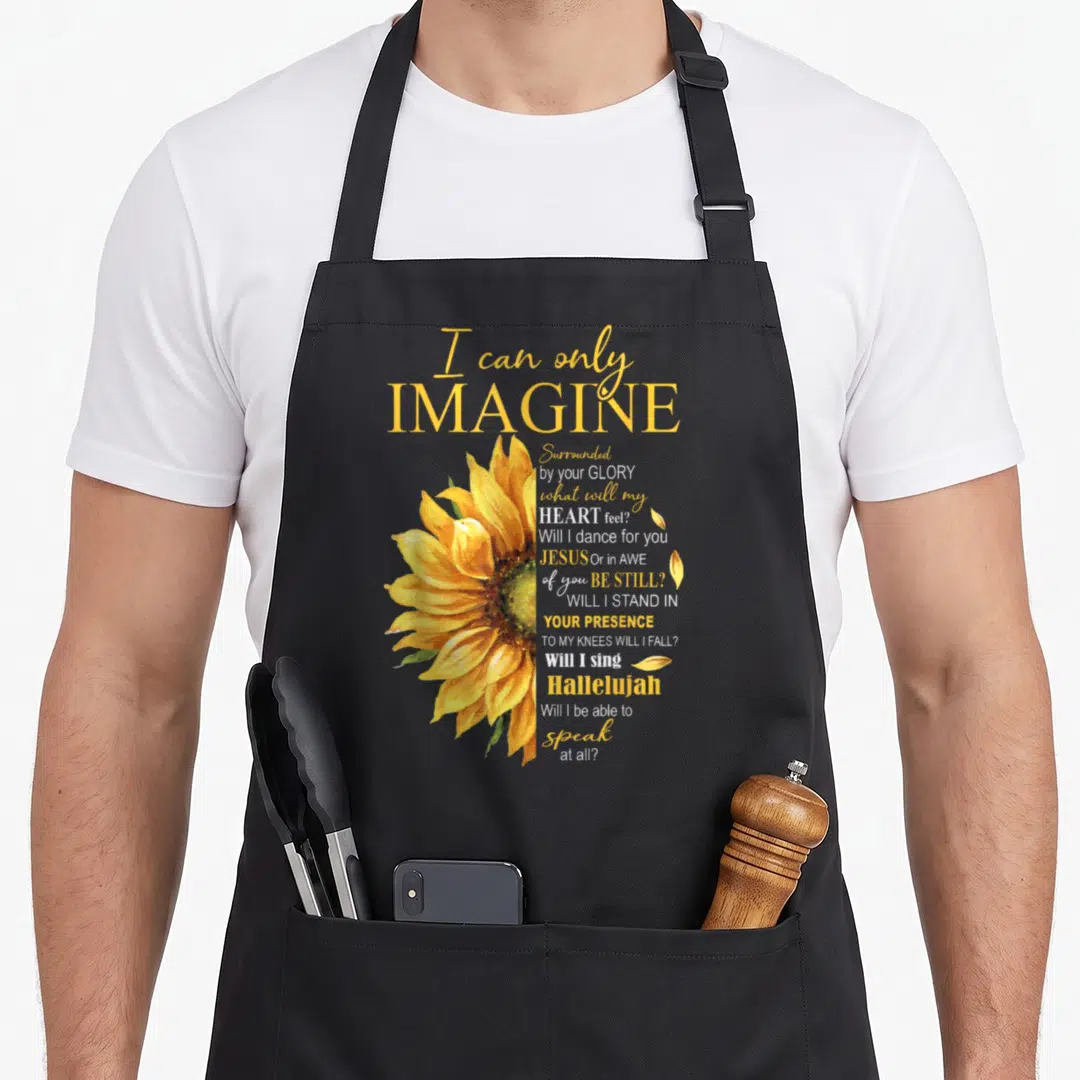 Imagine catholic apron - Yellow watercolor sunflower beside stacked I can only imagine lyrics in white and gold script — shown on a black cotton canvas apron against a white background