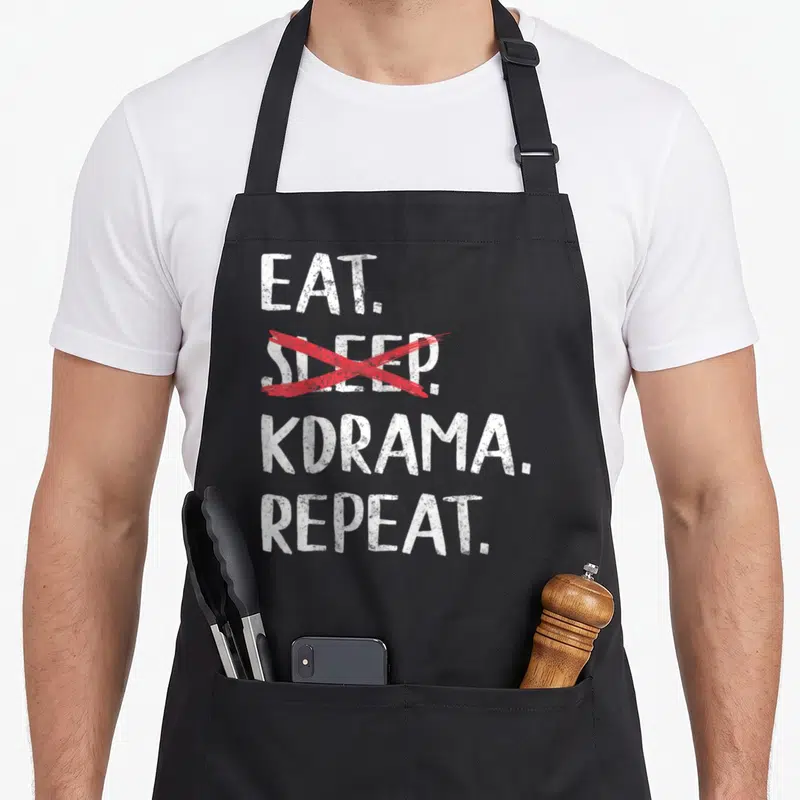 Eat jet girl apron - EAT SLEEP KDRAMA REPEAT text with red cross over sleep in white distressed font — shown on a black cotton canvas apron against a white background