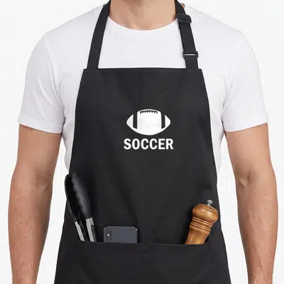 Irony football apron - White American football silhouette printed above the word SOCCER in minimalist style — shown on a black cotton canvas apron against a white background