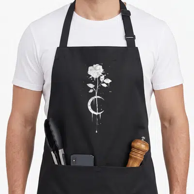 Occult rose apron - White distressed rose and crescent moon with dripping details on black background — shown on a black cotton canvas apron against a white background