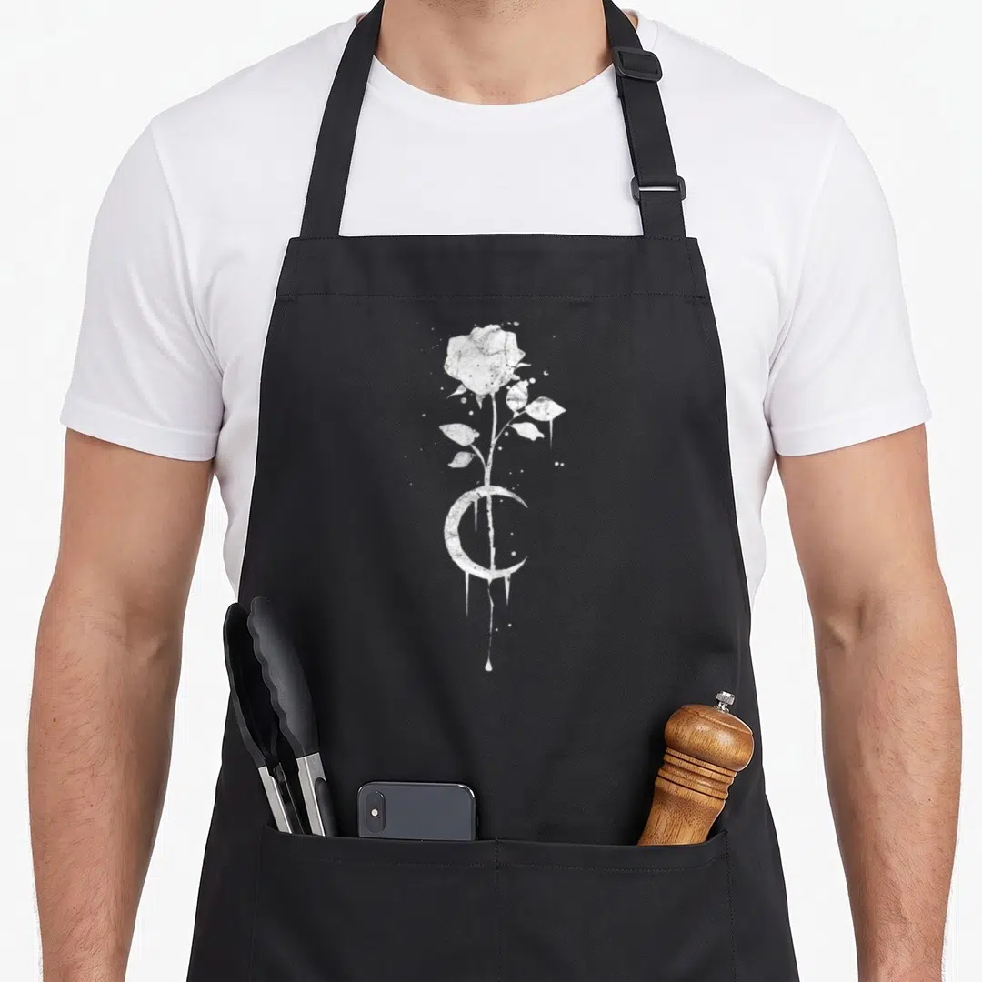 Occult rose apron - White distressed rose and crescent moon with dripping details on black background — shown on a black cotton canvas apron against a white background