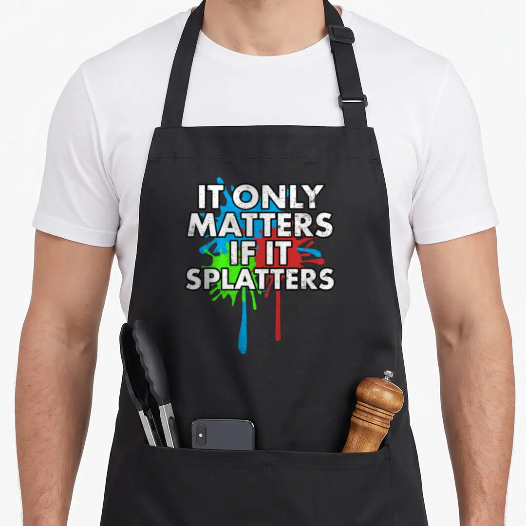 Paintball tactical apron - White text reading IT ONLY MATTERS IF IT SPLATTERS over blue red and green paint splatters — shown on a black cotton canvas apron against a white background