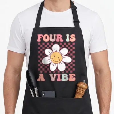 Four daisy apron - Smiling daisy on red pink checkerboard with Four Is A Vibe text — shown on a black cotton canvas apron against a white background