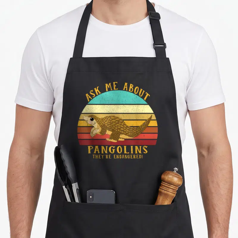 Save pangolin apron - Retro striped sun with pangolin illustration and text ASK ME ABOUT PANGOLINS THEY'RE ENDANGERED! — shown on a black cotton canvas apron against a white background