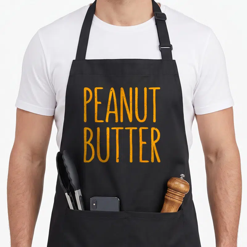 Costume butter apron - Orange distressed PEANUT BUTTER text stacked on grey background — shown on a black cotton canvas apron against a white background