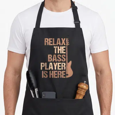 Guitarist bass apron - Copper distressed text stack next to a vertical bass guitar silhouette on a black apron — shown on a black cotton canvas apron against a white background