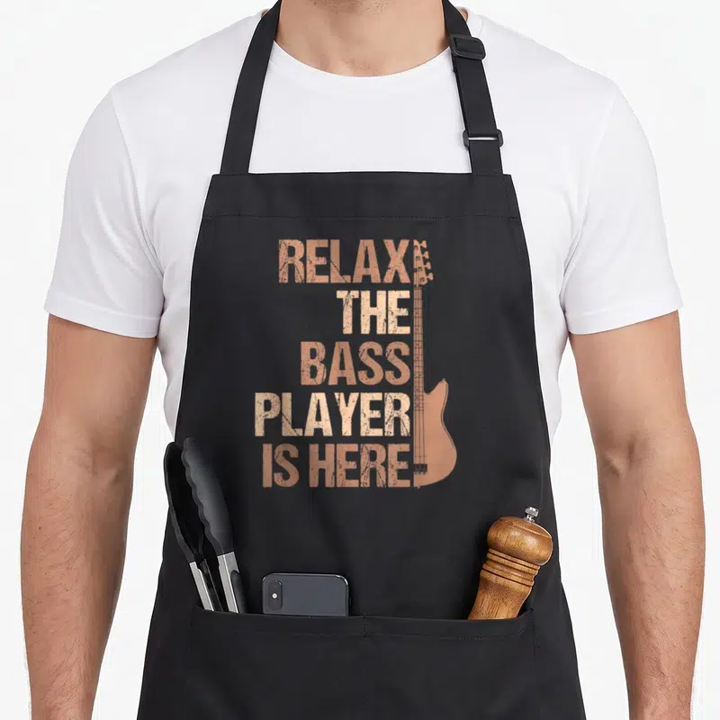 Guitarist bass apron - Copper distressed text stack next to a vertical bass guitar silhouette on a black apron — shown on a black cotton canvas apron against a white background