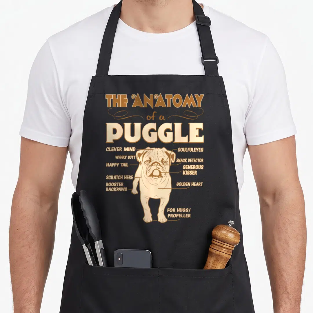 Puggle anatomy apron - Tan line art of a pug labeled with Snacks Detector and Golden Heart text — shown on a black cotton canvas apron against a white background
