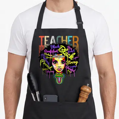 Teacher african apron - Cartoon woman face with colorful script words Black Proud Strong Melanin in afro hair — shown on a black cotton canvas apron against a white background
