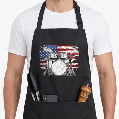 Drummer 4th of july apron - Distressed drum kit illustration overlaid on a grunge style American flag pattern — shown on a black cotton canvas apron against a white background