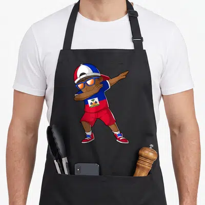Haitian heritage aprons - Cartoon boy dabbing in red blue white outfit with Haitian flag shirt and cap — shown on a black cotton canvas apron against a white background