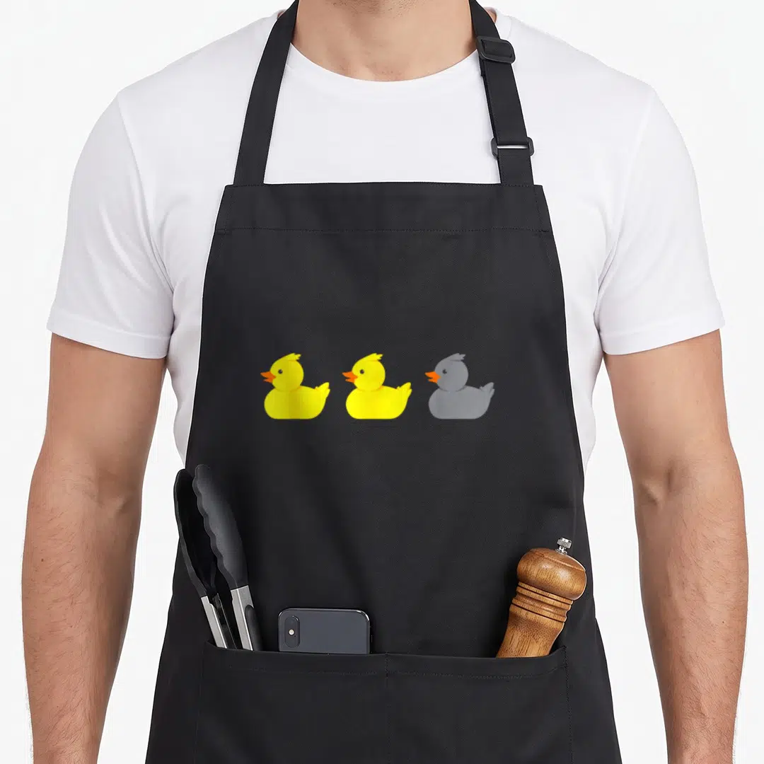 Funny duck minnesota apron - Three cartoon rubber ducks, two yellow and one grey, arranged horizontally with orange — shown on a black cotton canvas apron against a white background