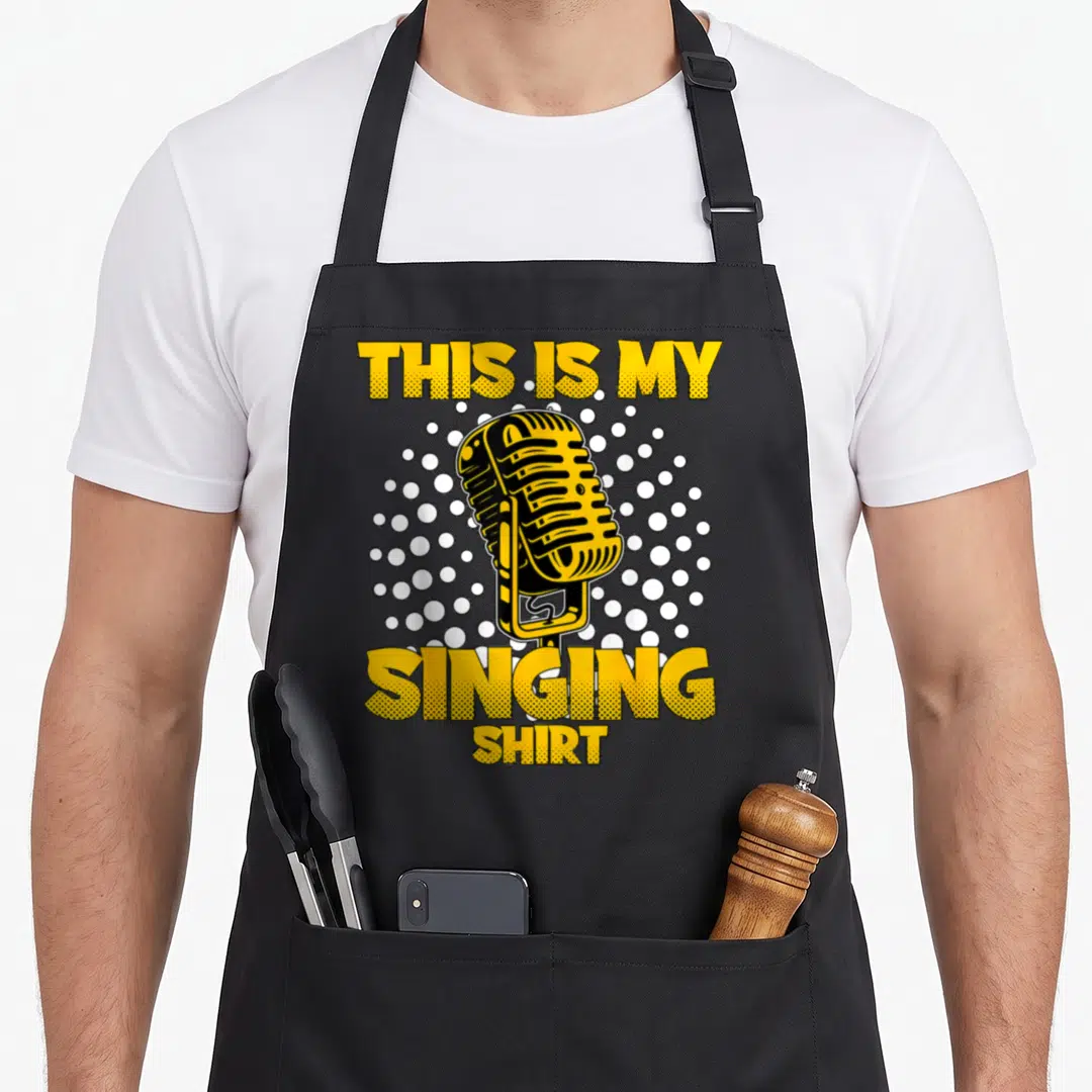 Karaoke singing addict apron - Retro yellow microphone between stacked text THIS IS MY SINGING SHIRT on white dot — shown on a black cotton canvas apron against a white background