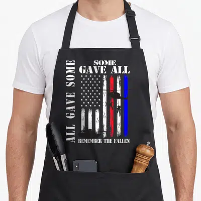 Gave family aprons - Distressed USA flag with helicopter soldiers tank and All Gave Some Some Gave All Remember — shown on a black cotton canvas apron against a white background